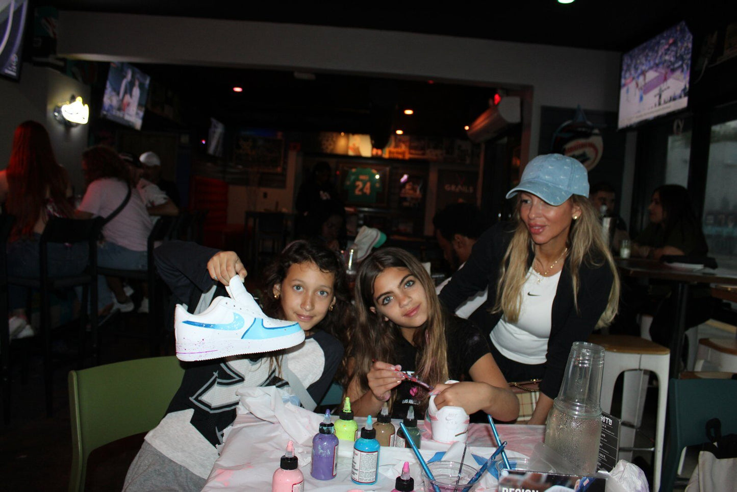 Smiling adult guests holding finished custom sneakers at Kick Art Workshop in Wynwood Miami